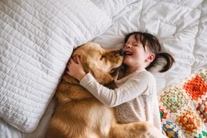 a young girl playing with her golden retriever on a bed