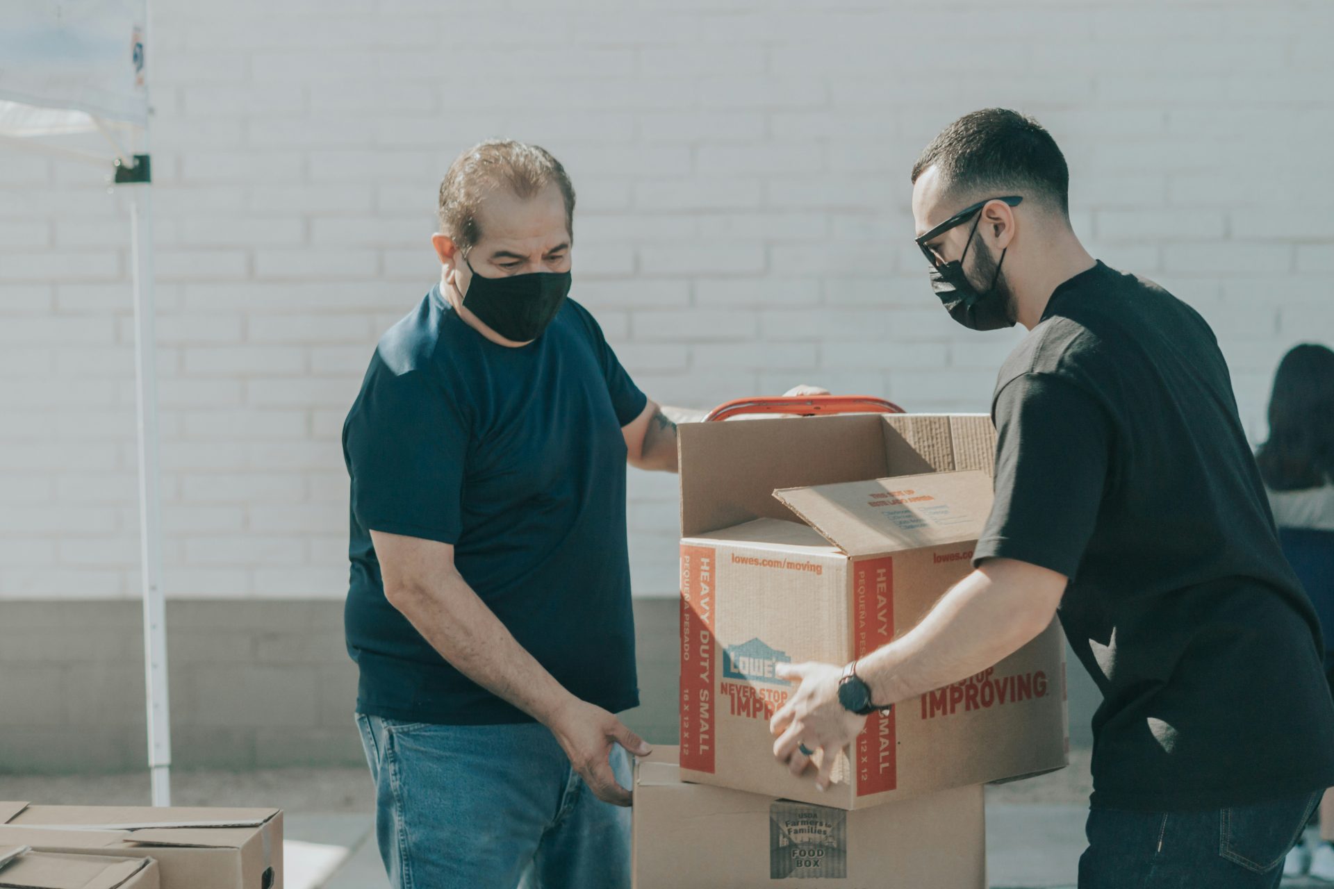 Two men moving cardboard boxes with face masks on 