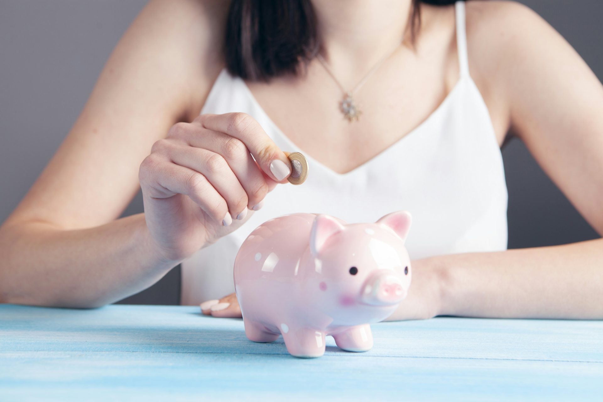 woman in white top putting a coin into a small piggy bank
